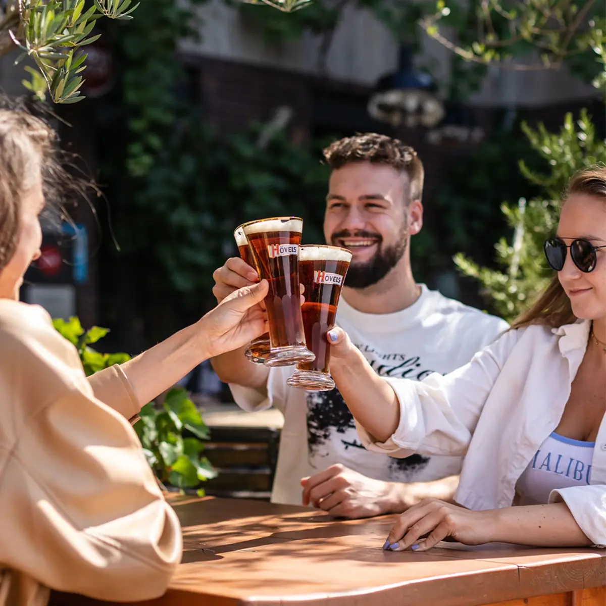 Drei Menschen stoßen im Freien mit Biergläsern an.