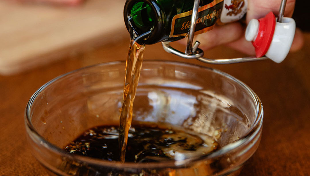 Sojasauce wird aus einer grünen Flasche in eine kleine Glasschale gegossen.