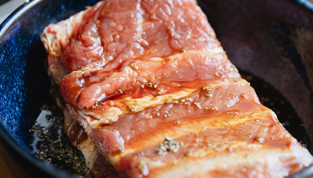 Gewürztes rohes Schweinefleisch liegt in einer blauen Schüssel.
