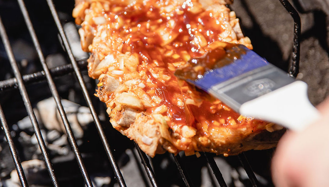 Ein mariniertes Stück Fleisch wird auf einem Grill gekocht und mit einer Sauce bestrichen.