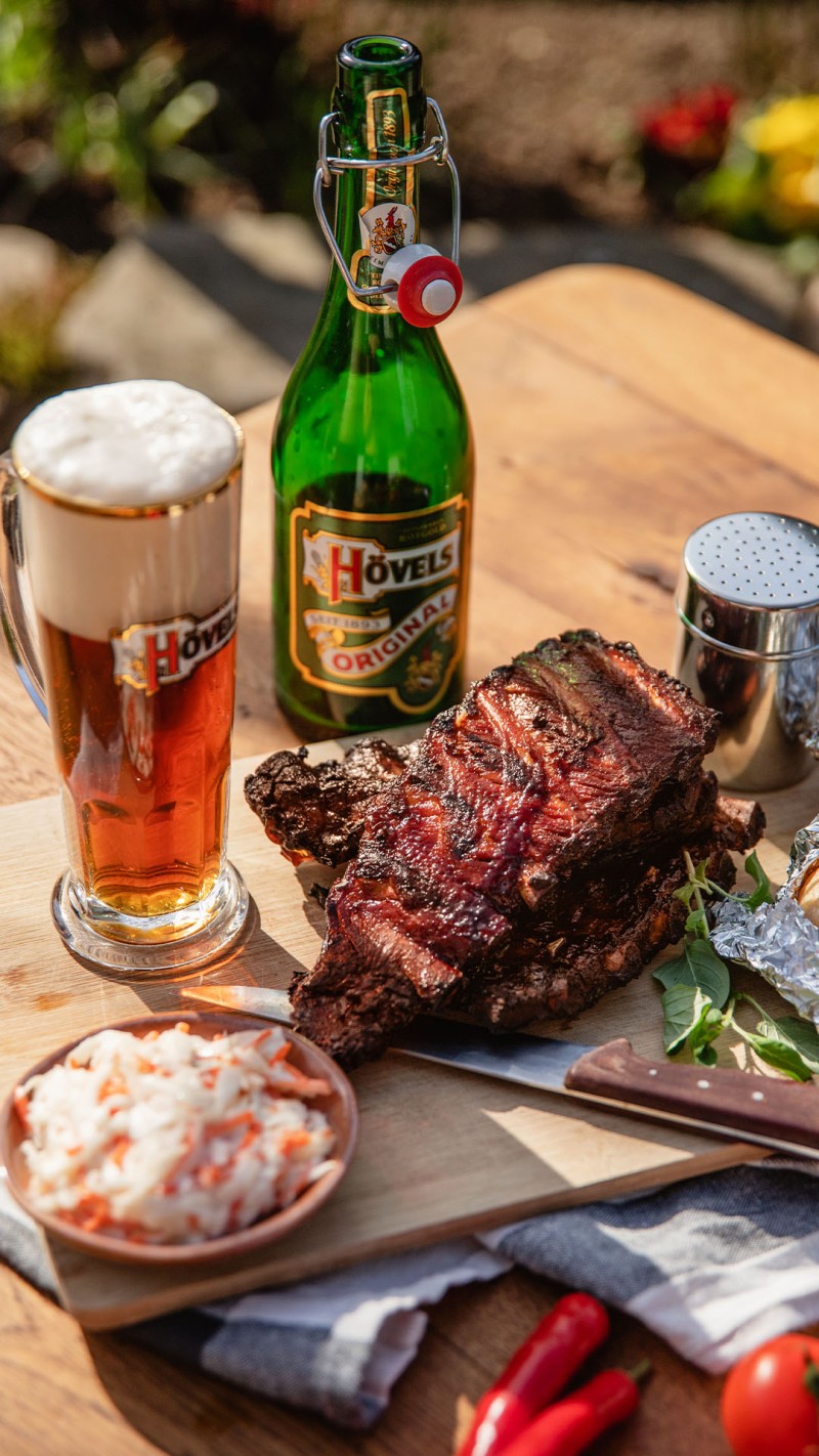 Ein Glas Bier steht neben einer Flasche und einem Teller mit gegrillter Rinderbrust und Salat.
