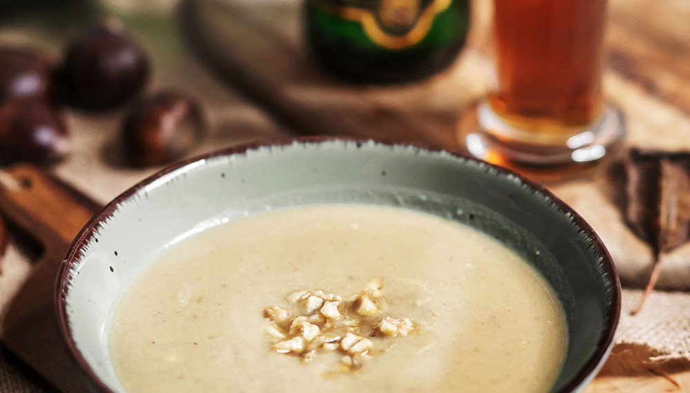 Eine Schüssel mit cremiger Suppe steht auf einem Holztisch, garniert mit Kernen.
