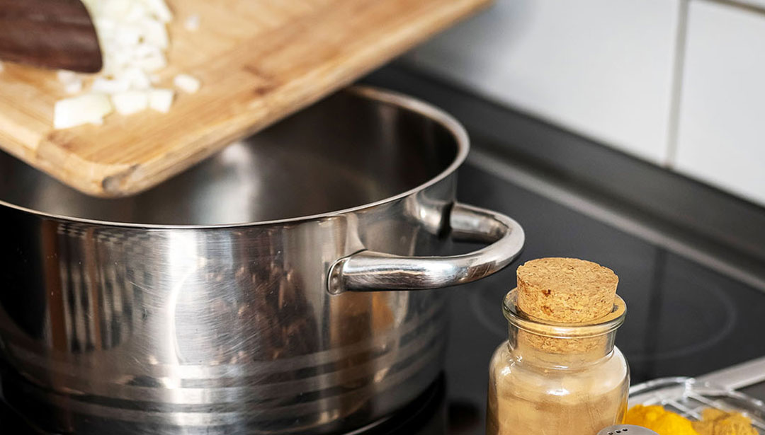 Ein Edelstahltopf steht auf einer schwarzen Herdplatte neben einem Glas mit Korkdeckel.