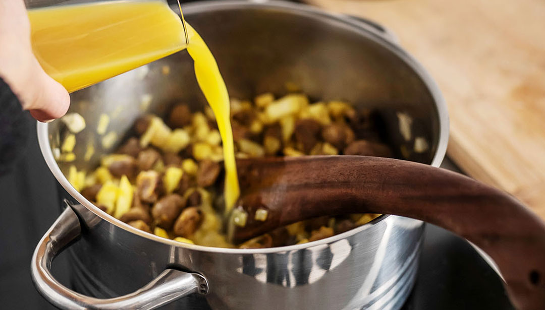 Eine Hand gießt Öl in einen Topf mit Kartoffeln und Pilzen.