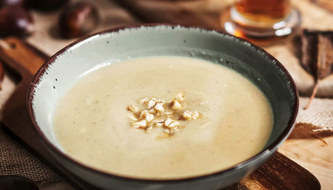 Eine Schale mit cremiger Suppe steht auf einem Holzbrett. Darin sind einige Körner gestreut.