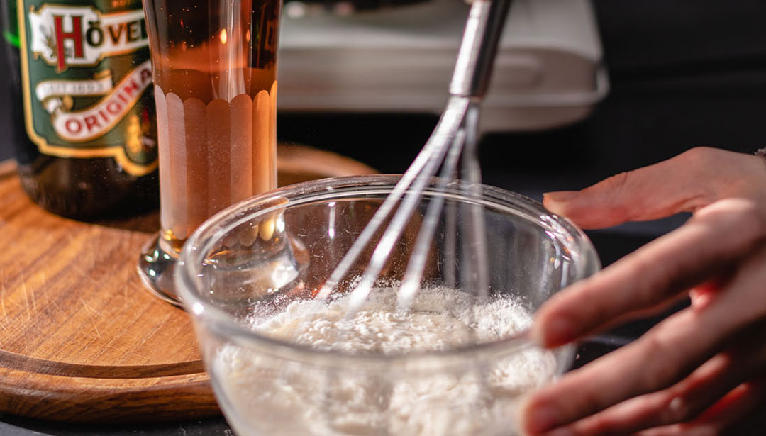 Eine Hand rührt mit einem Schneebesen Mehl in einer Glaschüssel.