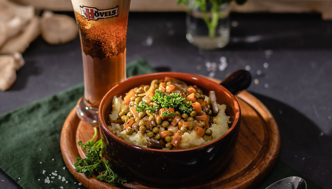 Ein Glas Bier steht neben einem Teller mit Linsengericht und Kartoffelpüree.