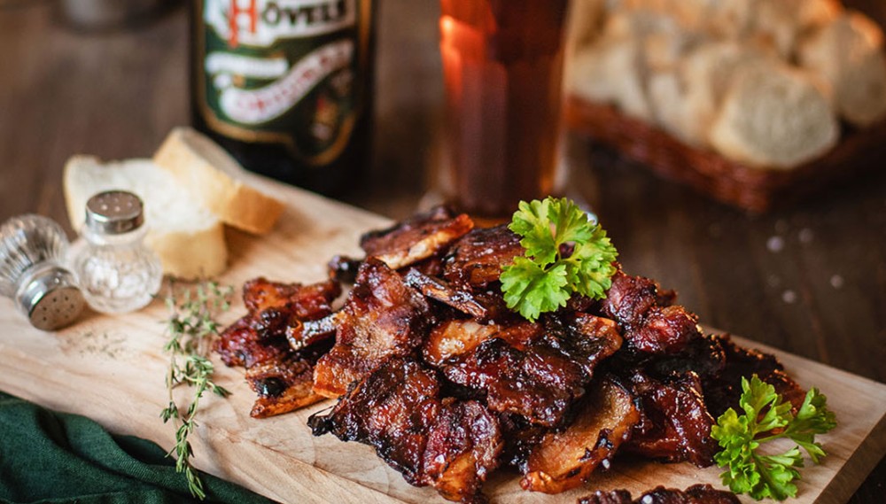 Geröstete Rippchen liegen auf einem Holzbrett garniert mit Petersilie.