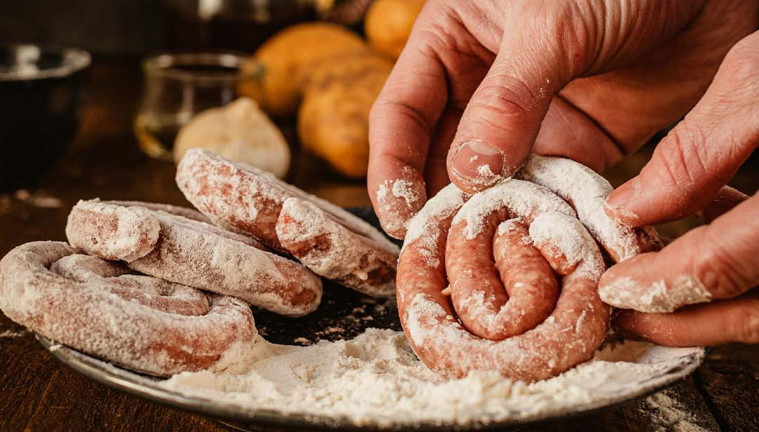 Eine Person bereitet rohes Wurstfleisch zu, das mit Mehl bestäubt ist.