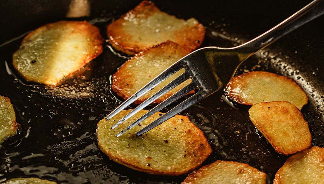 In einer Pfanne werden dünne Kartoffelscheiben gebraten und mit einer Gabel gewendet.