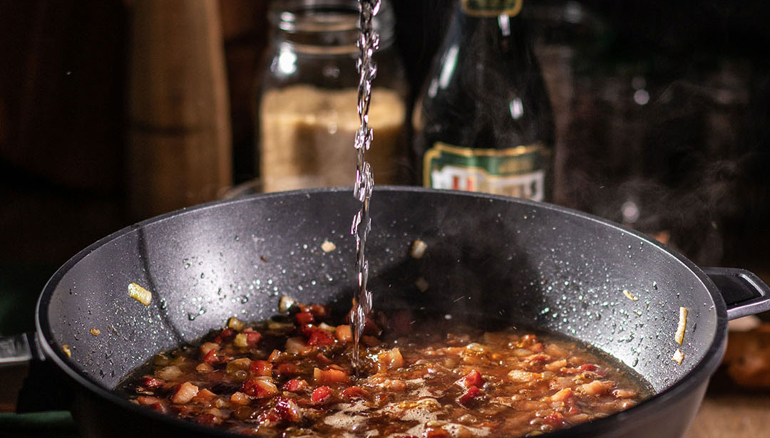 Wasser wird in eine Bratpfanne mit brutzelndem Gemüse und Fleisch gegossen.