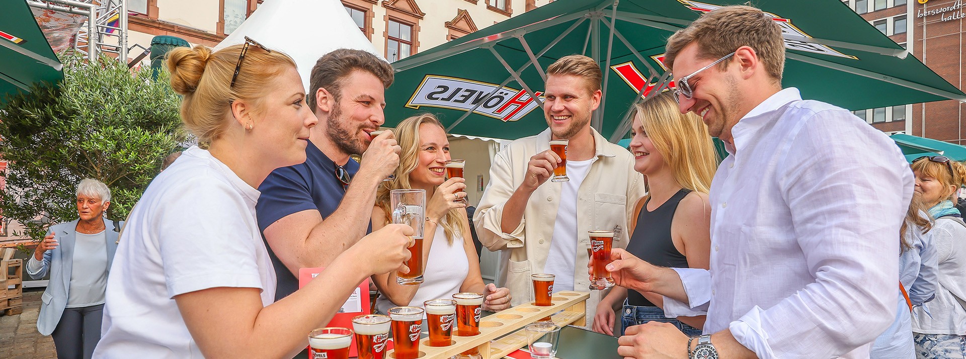 Mehrere Personen genießen gemeinsam Getränke an einem Außentresen bei Sonnenschein.